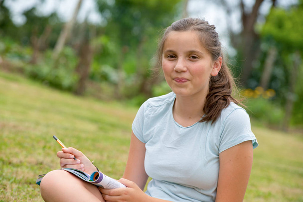 egy fiatal és mosolygós tinédzser keresztbetett lábbal ül a fűben - Fotó, kép
