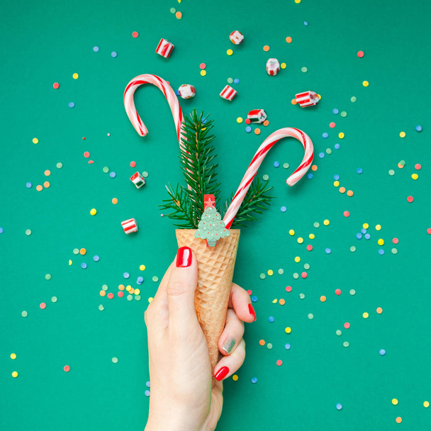 Boże Narodzenie Boże Narodzenie nowy rok wakacje celebracja dama ręka czerwony manicure trzyma wafel stożek cukierki laski jodła drzewo gałąź kopii przestrzeni zielony kolor tła papieru. Z życzeniami kwadratowych szablon 2019 - Zdjęcie, obraz