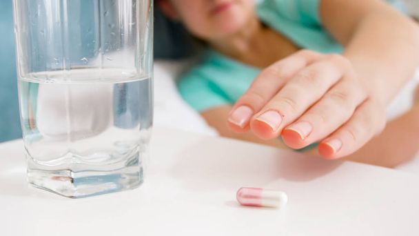Closeup image of female hand reaching for pill lying on bedside table - Zdjęcie, obraz