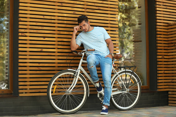 Handsome young hipster man with bicycle near wooden wall outdoors - Фото, зображення