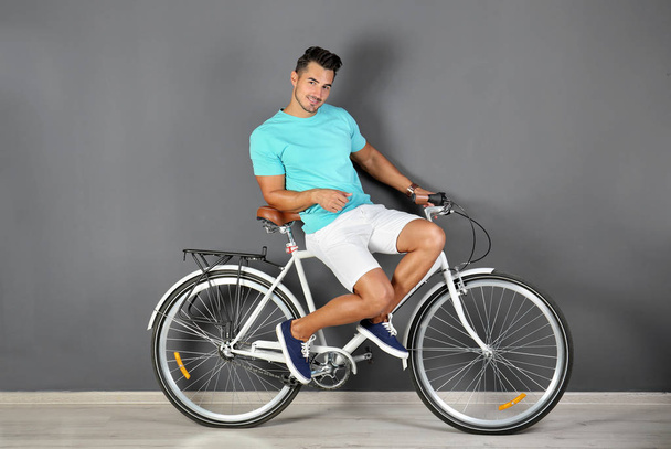 Handsome young hipster man with bicycle near color wall - Foto, Bild