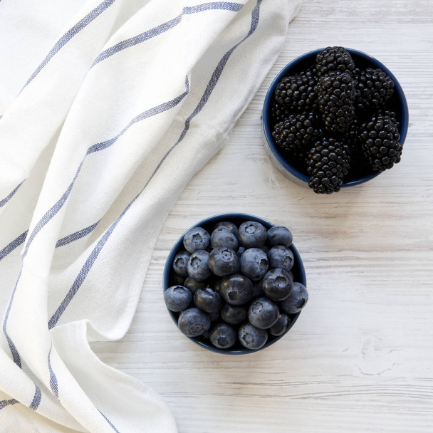 Full blue bowls of berries on a white wooden background, overhead view. From above, top view, flat lay. - Foto, Bild