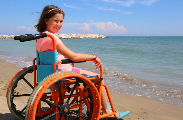 Yaz aylarında deniz kenarında tekerlekli sandalyedeki sevimli küçük kız - Fotoğraf, Görsel