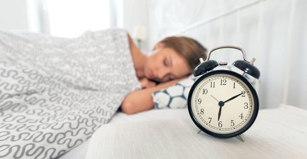Young woman is sleeping in her bed. Alarm clock in the foreground - Foto, Imagen
