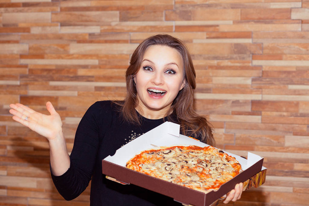 Adult woman holding box with pizza and looking super amazed and happy isolated on wood wall background - Фото, зображення