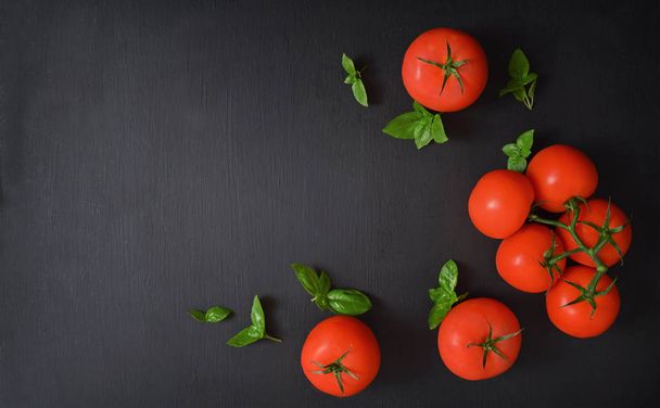Verse tomaten op een donkere achtergrond. Tomaten, peterselie, dille, tomaten en basilicum op een donkere achtergrond. Bovenaanzicht. Voedsel achtergrond. - Foto, afbeelding