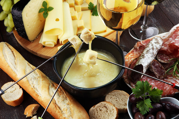 Gourmet Swiss fondue dinner on a winter evening with assorted cheeses on a board alongside a heated pot of cheese fondue with two forks dipping bread and white wine behind in a tavern or restaurant - Photo, Image