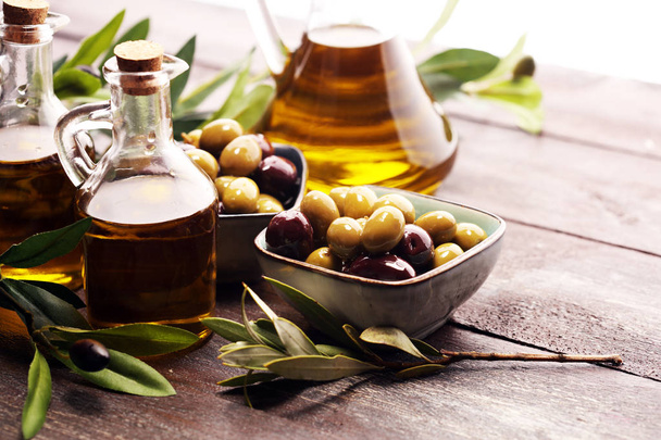 Fles vergine olijfolie en olie in een kom met olijven. - Foto, afbeelding
