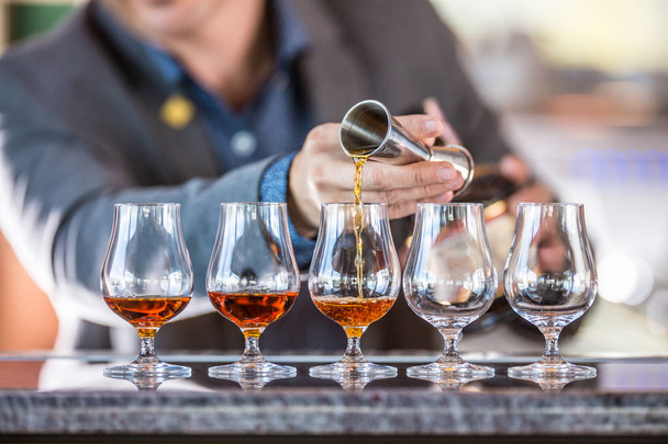 Bartender professional voorbereiding van vijf alcololic dranken. Hij gieten een zeer hoge kwaliteit rum of cognac. - Foto, afbeelding