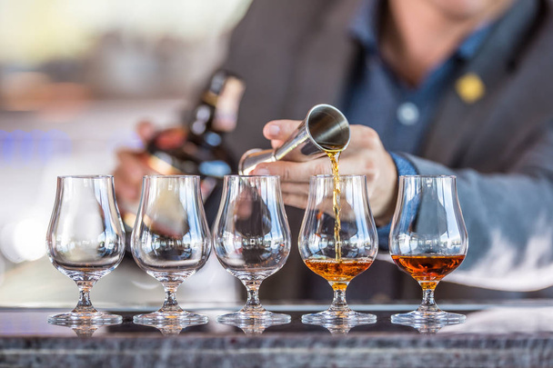 Bartender professional preparing five alcololic drinks. He pouring a very high quality rum or cognac. - Foto, Imagem