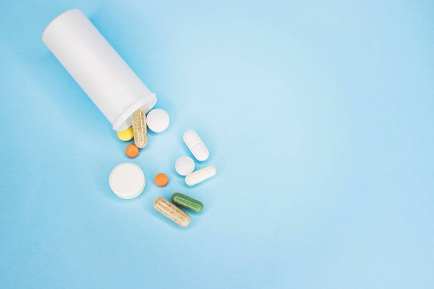 Omega 3 visolie capsules morsen uit witte plastic fles op een blauwe achtergrond. - Foto, afbeelding