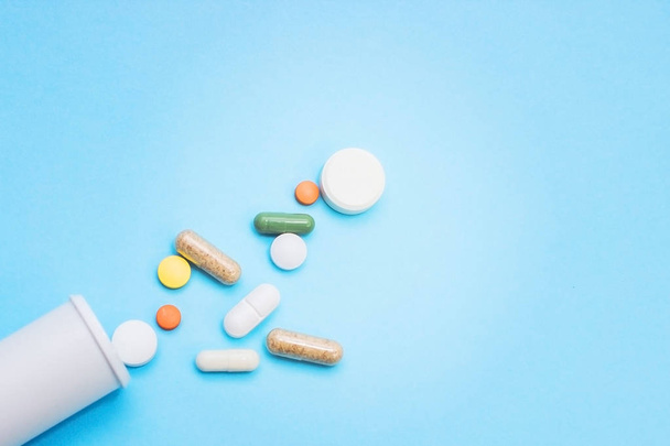 Çok renkli tablet ve kapsül, tablet, ilaç tıp hapları üzerinde mavi arka plan, analjezik hastalıklara karşı beyaz şişe - Fotoğraf, Görsel