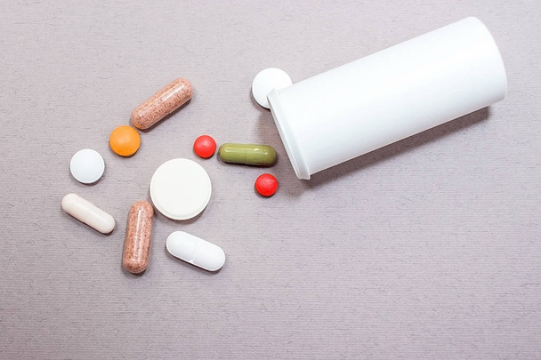Tabletten auf grauem Hintergrund, eine Flasche mit Tabletten auf grauem Hintergrund in verschiedenen Farben, Medikamente auf grauem Hintergrund. - Foto, Bild