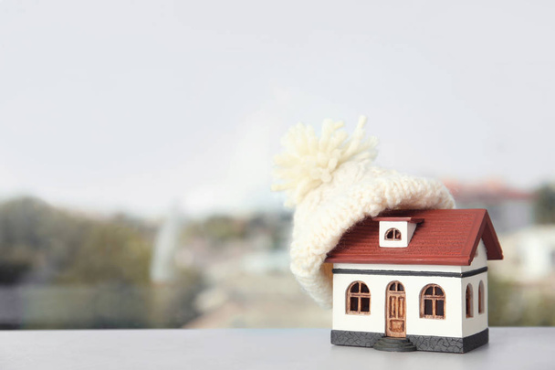 House model with knitted hat on table against blurred background, space for text. Heating concept - Фото, зображення