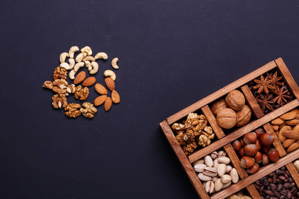 Assortment of nuts in a wooden box on a black background - healthy snack. Top view. Copy space - Fotoğraf, Görsel