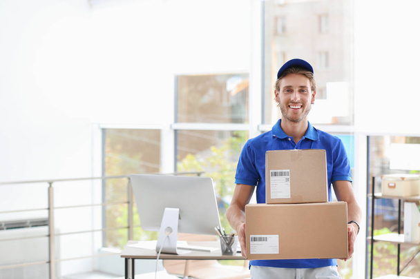 Young courier standing with parcels near office desk. Space for text - Foto, Imagem