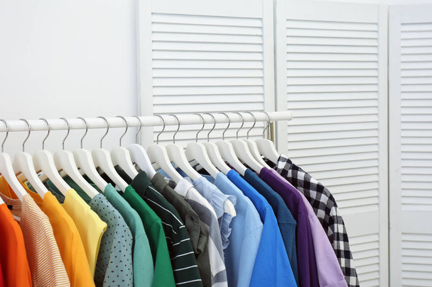 Rack with bright clothes in room. Rainbow colors - Φωτογραφία, εικόνα