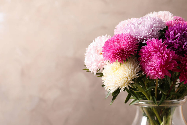 Beautiful aster flower bouquet in vase on color background. Space for text - Foto, afbeelding