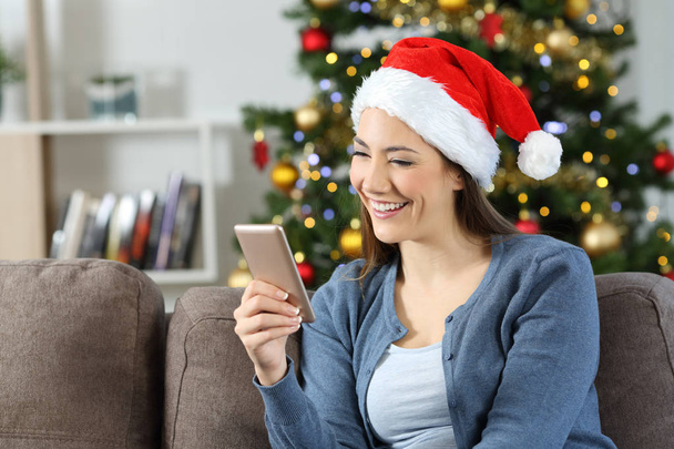 Girl reading phone messages in christmas sitting on a couch in the living room at home - Foto, Imagem
