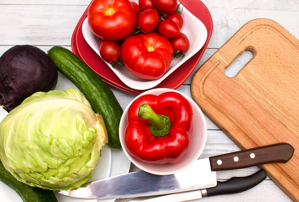 Conjunto de verduras diversas, productos alimenticios saludables (tomates, pimiento dulce, col, pepinos) y tabla de cortar con cuchillos
. - Foto, imagen