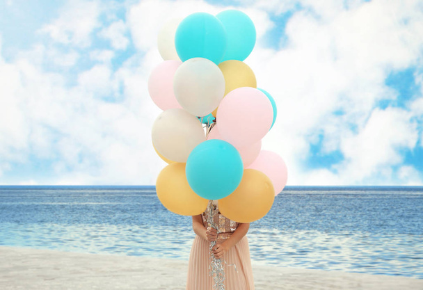 Young woman holding bunch of balloons outdoors - Foto, afbeelding