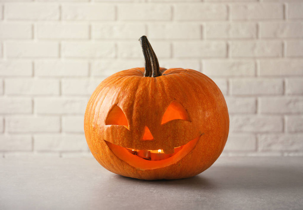 Halloween pumpkin head jack lantern on table against brick wall - Fotó, kép