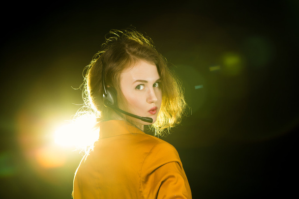 Young beautiful woman-operator with headphone smiles, it is isolated on black background. - Foto, Imagem