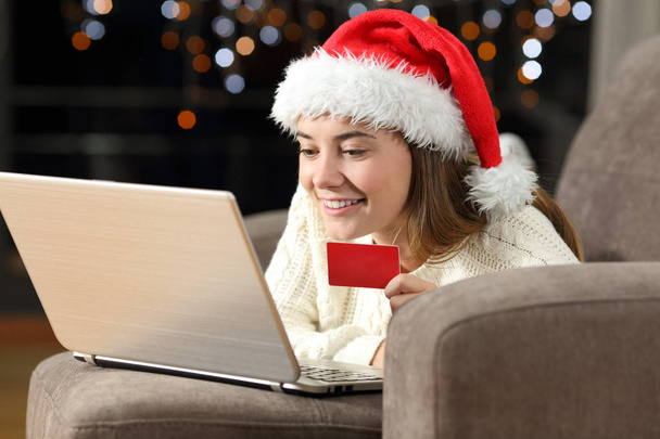 Happy teen buying on line with a phone and credit card in christmas lying on a couch in the living room at home - Fotoğraf, Görsel