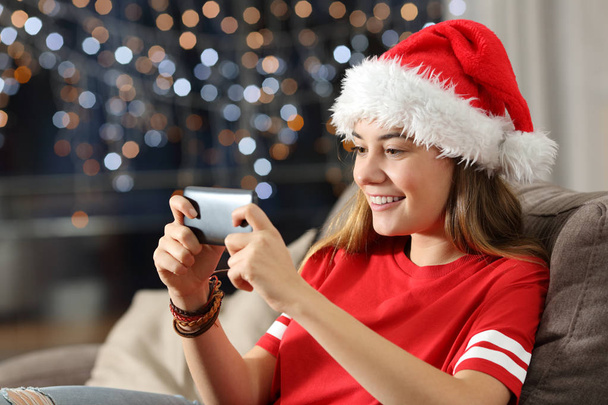 Підліток дивиться медіа на смартфон в Різдво сидить на дивані у вітальні вдома
 - Фото, зображення