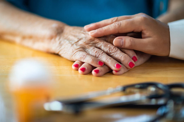 Fiatalabb női kéz érintése idősebb felnőtt nő kezében sztetoszkóp és orvosi üveg közelében. - Fotó, kép