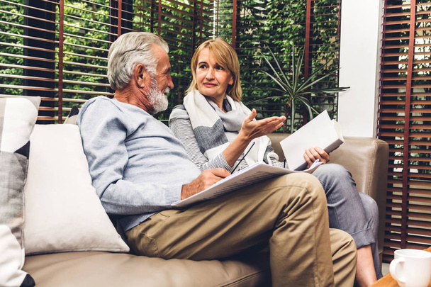 Üst düzey çift konuşmak ve evde oturma odasında kanepede birlikte gazete okuma rahatla. Emeklilik çift kavramı - Fotoğraf, Görsel