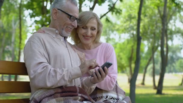Grandfather and grandmother admiring children photos in smartphone application - Filmati, video