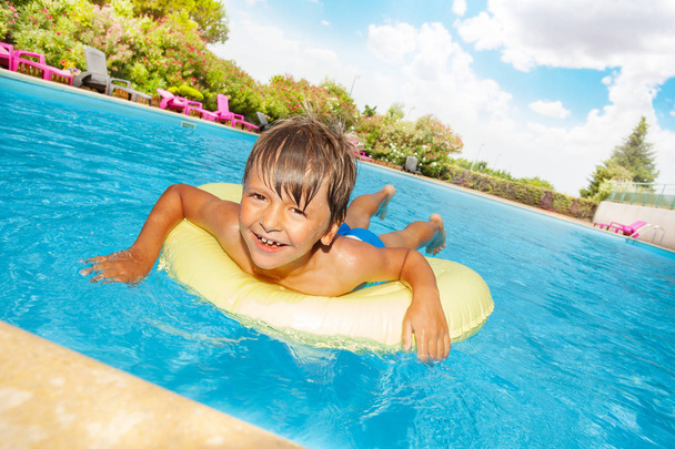 Portrait of happy boy floating on yellow swim tube in the swimming pool and looking at camera - Фото, зображення