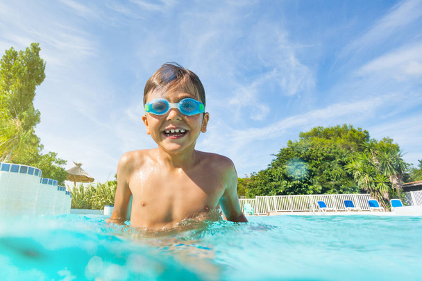 Portrait of wet boy in goggles, standing in the swimming pool, laughing and enjoying summer - Zdjęcie, obraz