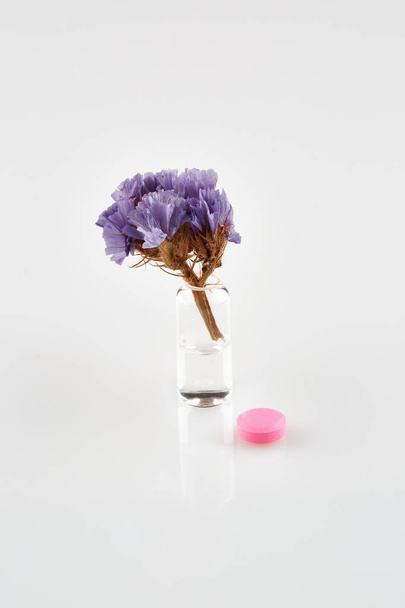 Violet flower in ampoule with medicine and red tablet. - Photo, Image