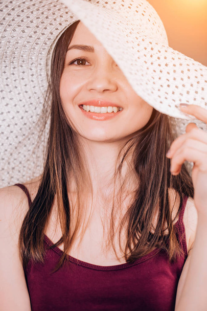 Portrait of an attractive brunette woman in a beige hat in the sun. Young girl looks with a smile at the camera - Foto, Imagem