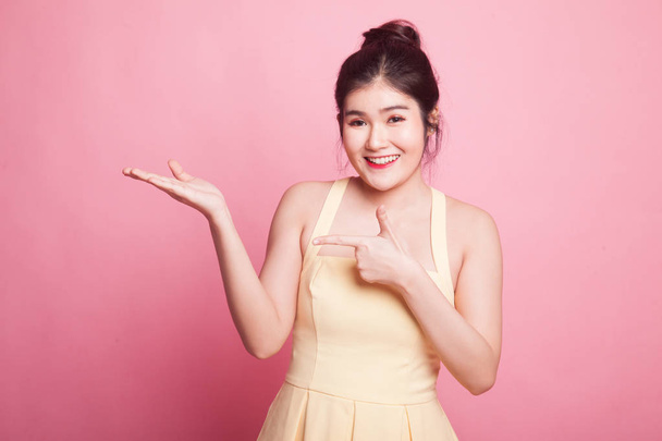 Beautiful young Asian woman point to palm hand on pink background - Foto, imagen