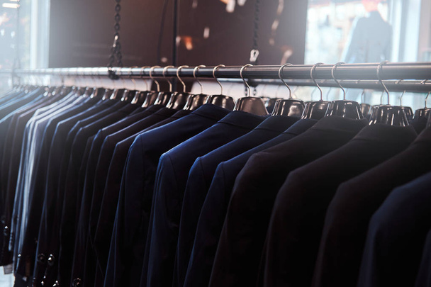Photo d'un rack avec des vestes de costume dans un magasin de vêtements pour hommes
. - Photo, image