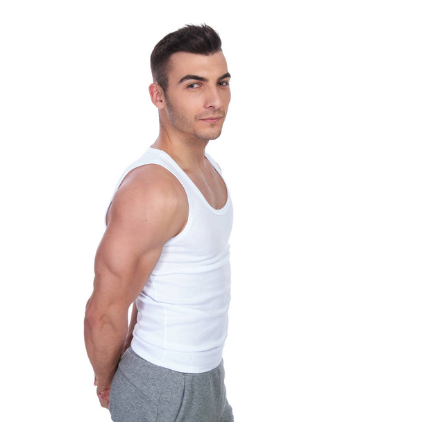 side view of sexy gym man wearing a white top flexing his triceps while standing on white background - 写真・画像