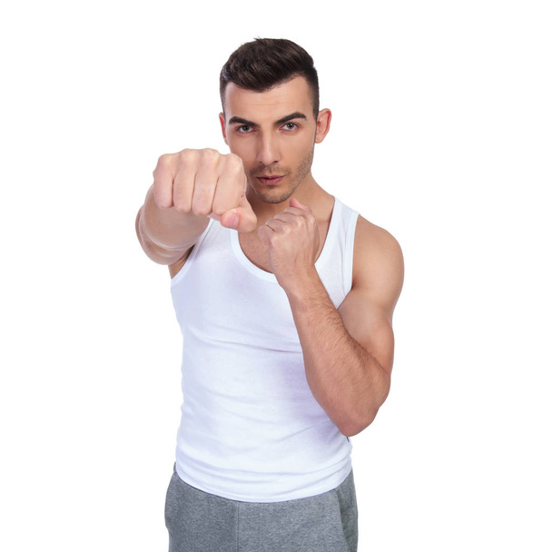 portrait of young boxer in undershirt punching forward while standing on white background - Foto, Imagen