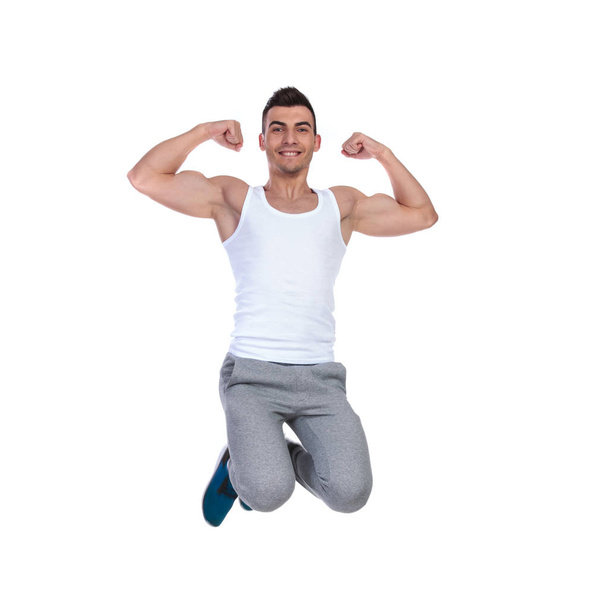 atractivo hombre musculoso saltando sobre fondo blanco y flexionando sus bíceps, imagen de cuerpo completo
 - Foto, Imagen