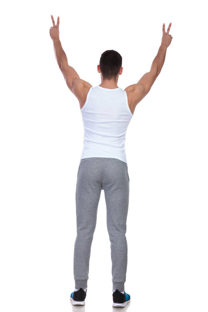vista trasera del hombre en camiseta celebrando con las manos en el aire y haciendo señal de paz mientras está de pie sobre fondo blanco
 - Foto, imagen