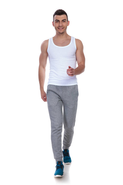 lachende fitness man in de witte onderhemdje lopen op witte achtergrond, volledige lichaam afbeelding - Foto, afbeelding