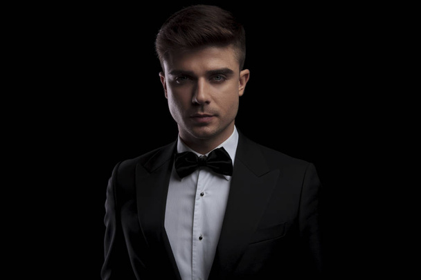 Porträt eines attraktiven eleganten Mannes, der einen schwarzen Anzug trägt und auf schwarzem Hintergrund steht - Foto, Bild