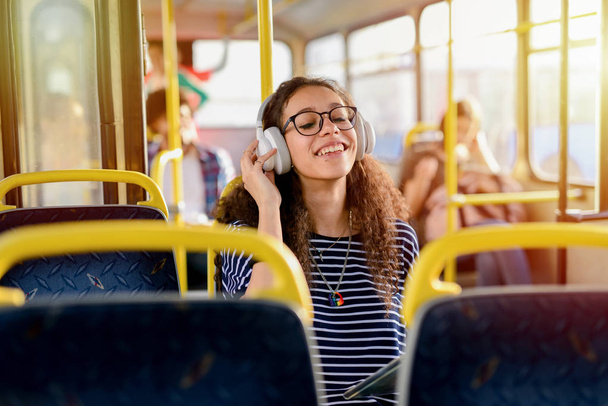 Bela menina estudante encaracolado sentado em um ônibus e ouvir a música em seu caminho para a escola
. - Foto, Imagem