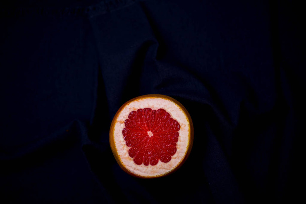 beautiful bright juicy piece of red grapefruit on a black background in the middle bottom of the black dark background with copy space - Foto, Imagen