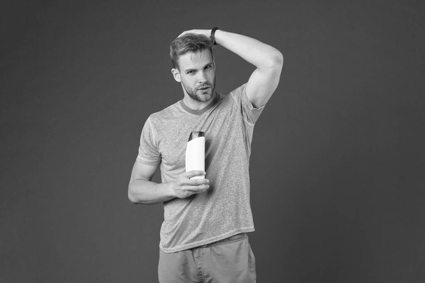 Man on confident face touching his hair, violet background. Guy with bristle holds bottle with shampoo, copy space. Hair care and shampoo concept. Man enjoy freshness after washing hair with shampoo - Foto, imagen