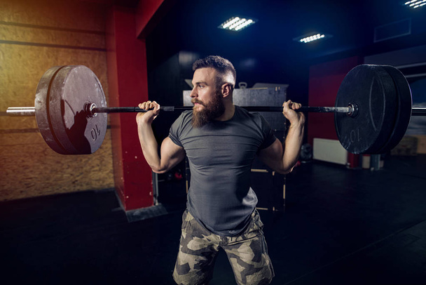 Bearded strong sporty man lifting heavy weight in dark room. - Zdjęcie, obraz