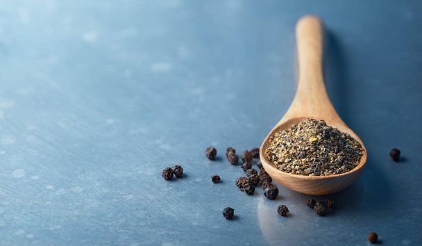Wooden spoon filled with ground pepper and Black Peppercorns  - Foto, afbeelding