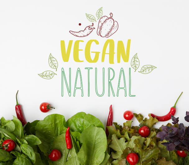 vista superior de verduras frescas de varias hojas con tomates y pimientos en la superficie blanca con letras "veganas naturales"
 - Foto, Imagen